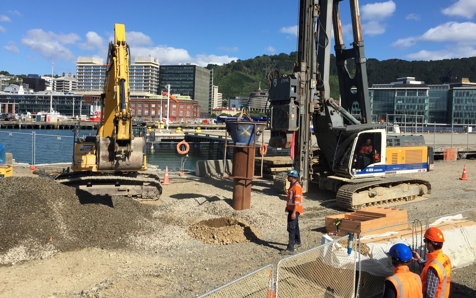 A drilling rig prepares the ground for piling on the port boundary while workers watch 