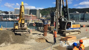 A drilling rig prepares the ground for piling on the port boundary while workers watch 